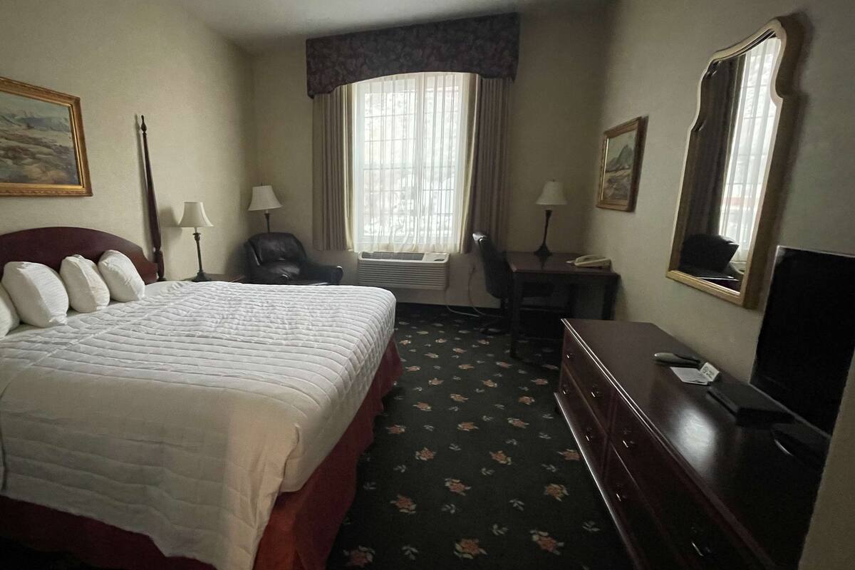 Une chambre d’hôtel avec un grand lit, un bureau, une chaise, une télévision et une fenêtre avec des rideaux.