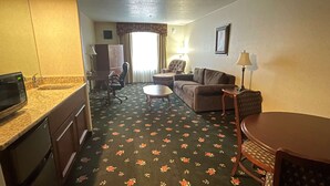 A hotel room with a kitchenette, a sofa, a chair, a small table, and a lamp. - Surestay Hotel By Best Western Eureka (Eureka)