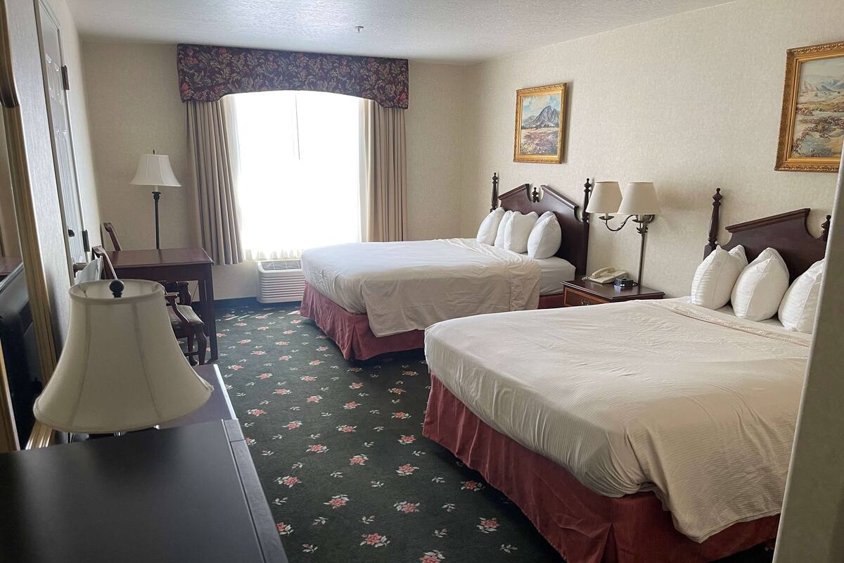 Une chambre d’hôtel avec deux lits, un bureau, une chaise, une lampe, un téléphone et un tableau au mur.