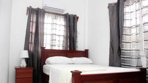 A bedroom with a wooden bed, a nightstand, a lamp, and a window with curtains.