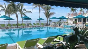 A pool area with lounge chairs and umbrellas, surrounded by palm trees. - P14 - Charming 2 Bedroom, 2 bath waterfront duplex with Cabana Club. (Key Colony Beach)