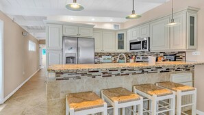 A modern kitchen with white cabinetry, a granite island with bar stools, stainless steel appliances, and pendant lighting. - P14 - Charming 2 Bedroom, 2 bath waterfront duplex with Cabana Club. (Key Colony Beach)