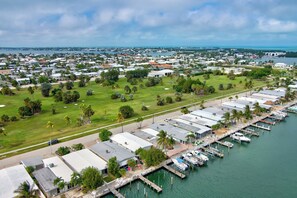 A marina with multiple boats docked, a golf course, and residential buildings in the background.