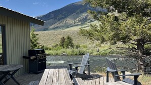A wooden deck with picnic tables and chairs overlooking a river and mountains. - Pagenkopf House on the Madison River (Cameron)