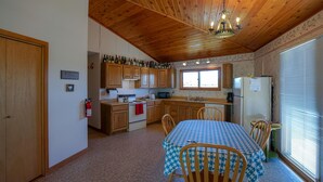 A kitchen with wooden cabinets, a stove, and a dining table with chairs. - Pagenkopf House on the Madison River (Cameron)