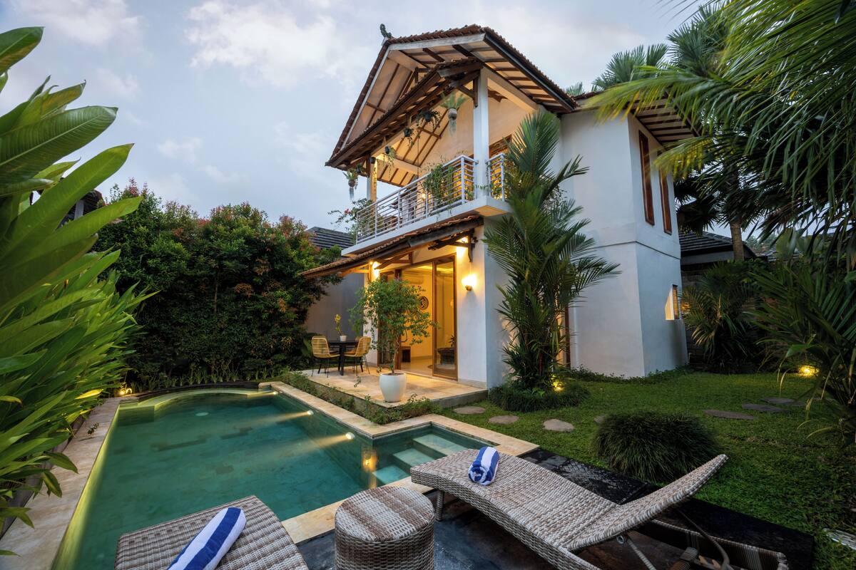 A two-story house with a swimming pool, outdoor seating, and lush greenery.
