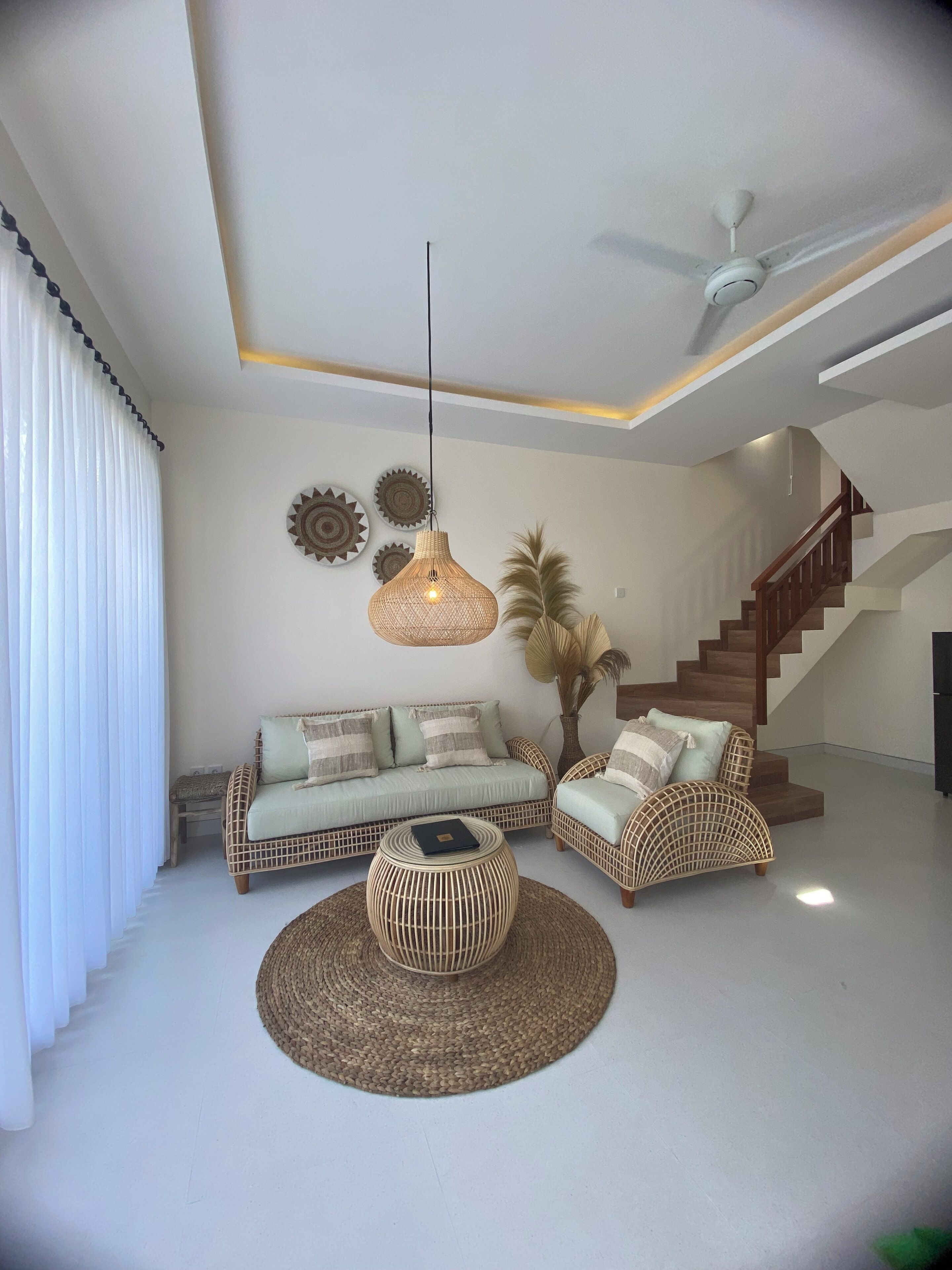 Uma sala de estar moderna com um sofá, duas poltronas, uma mesa de centro e um ventilador de teto.
