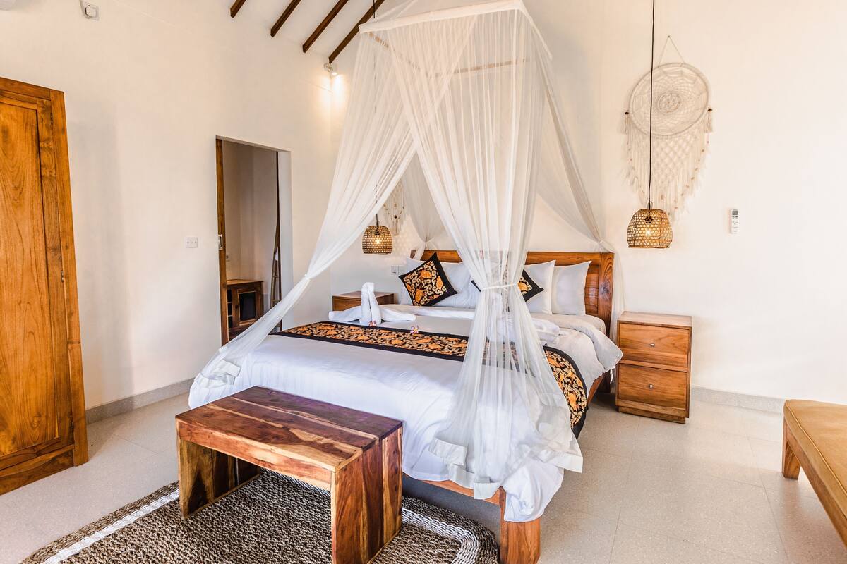 A bedroom with a four-poster bed, wooden nightstands, a bench, a woven rug, and a dreamcatcher on the wall.