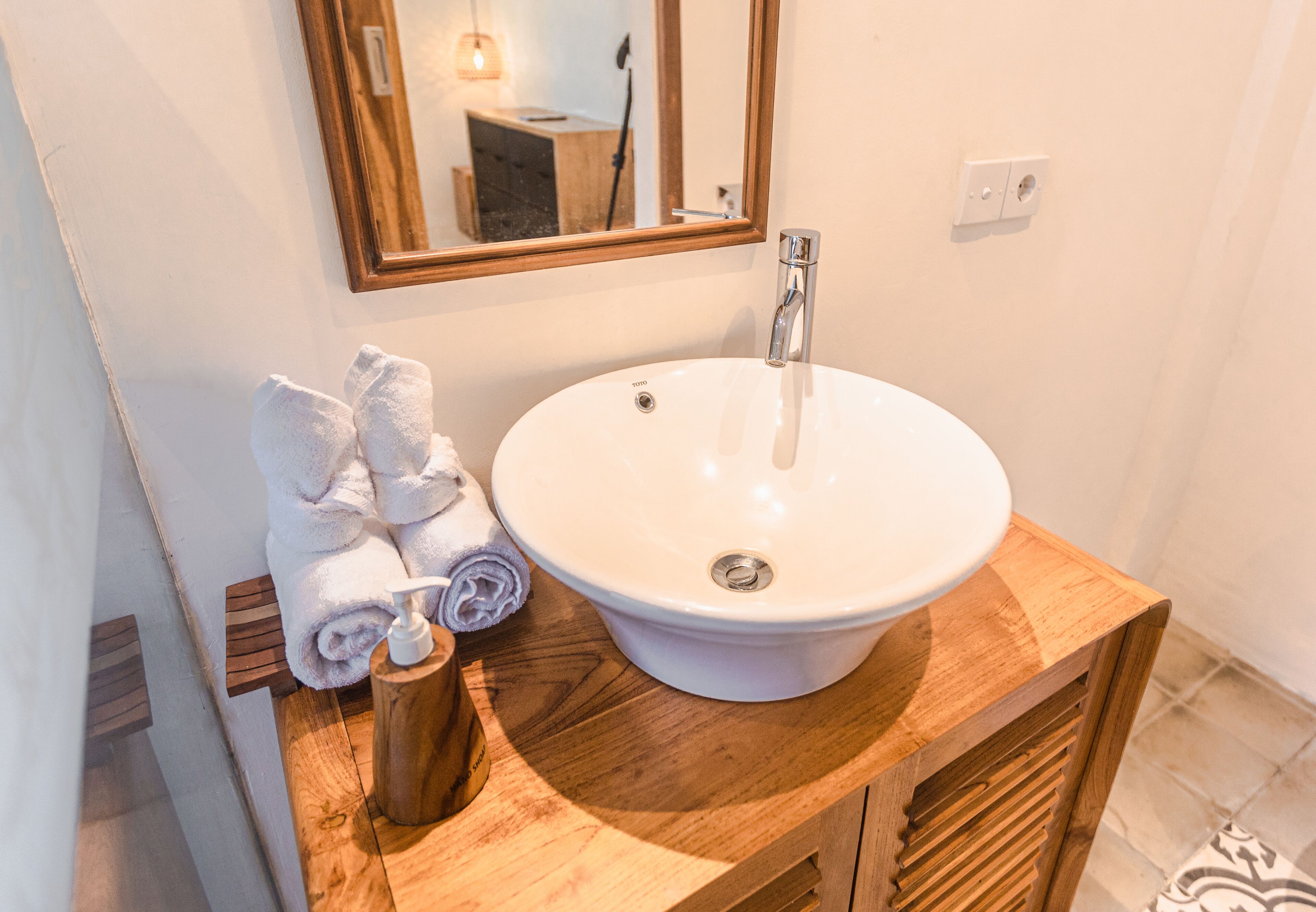 A bathroom with a white sink, wooden vanity, and a mirror.