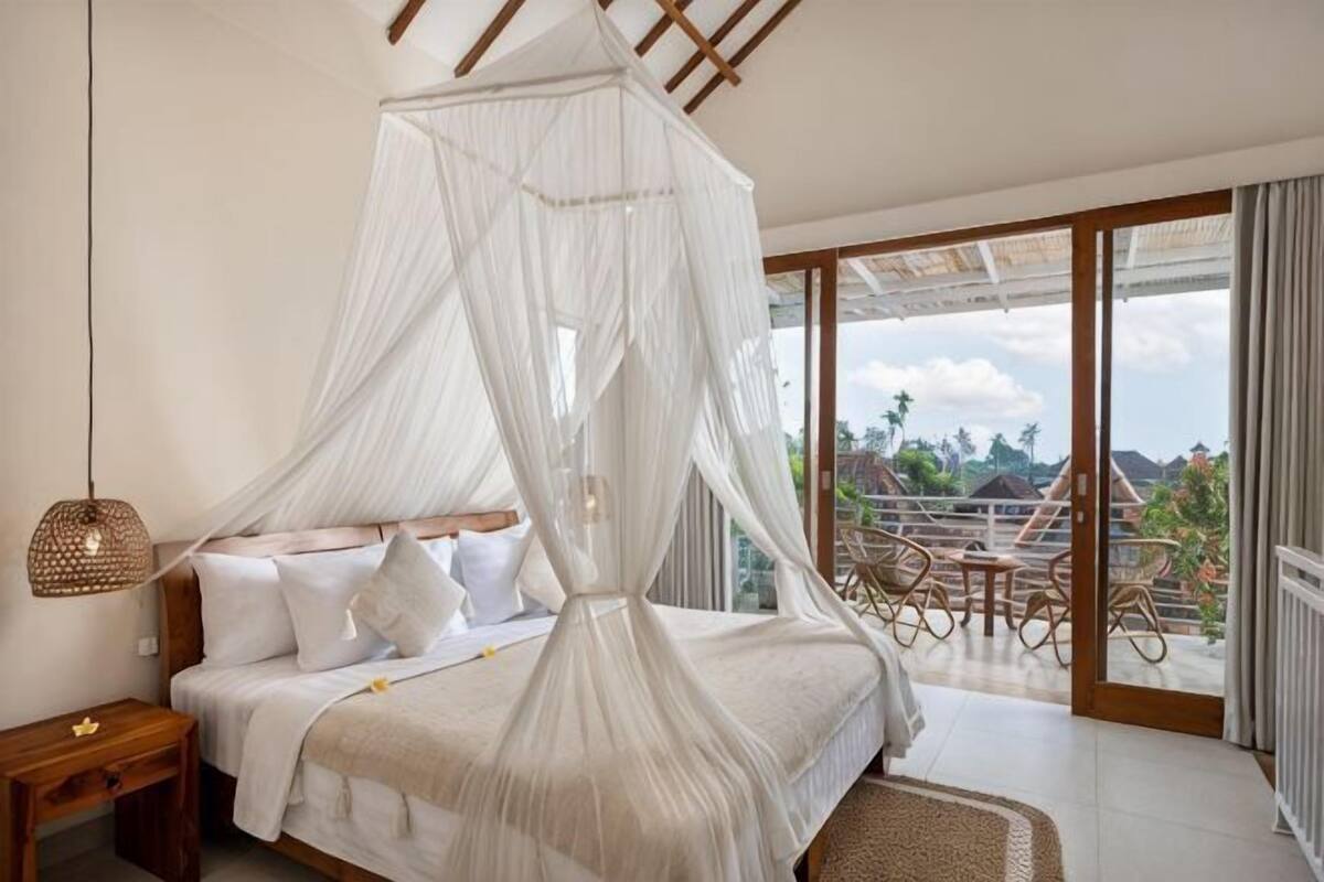 A bedroom with a canopy bed, a nightstand, and a view of the outdoors.