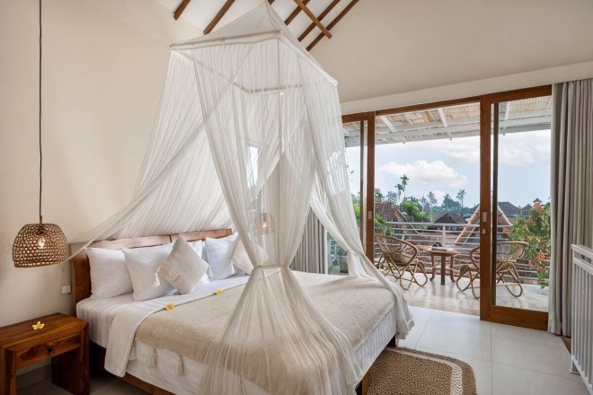 A bedroom with a canopy bed, a nightstand, and a view of the outdoors.