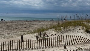 A sandy beach with a wooden fence, a clear sky, and the ocean in the background. - Beautiful Southwinds condo, oceanfront community with two pools and beach access (Atlantic Beach)