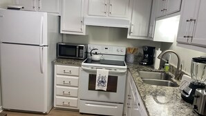 A kitchen with white cabinets, a microwave, a stove, a refrigerator, and a granite countertop. - Beautiful Southwinds condo, oceanfront community with two pools and beach access (Atlantic Beach)