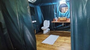 A compact, tent-like room with a wooden floor, a white toilet, and a small sink with a mirror.