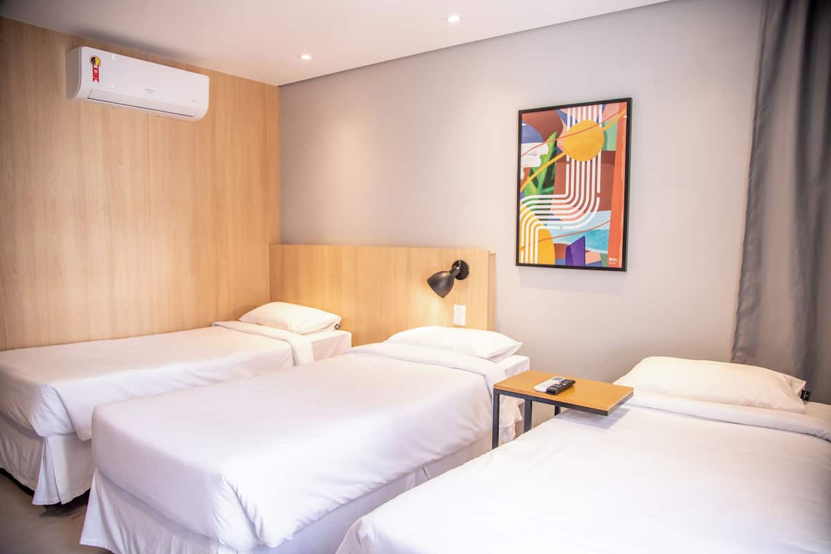 Une chambre d’hôtel avec deux lits, une tête de lit en bois, une peinture abstraite moderne, une table de chevet avec une lampe et un appareil de climatisation.