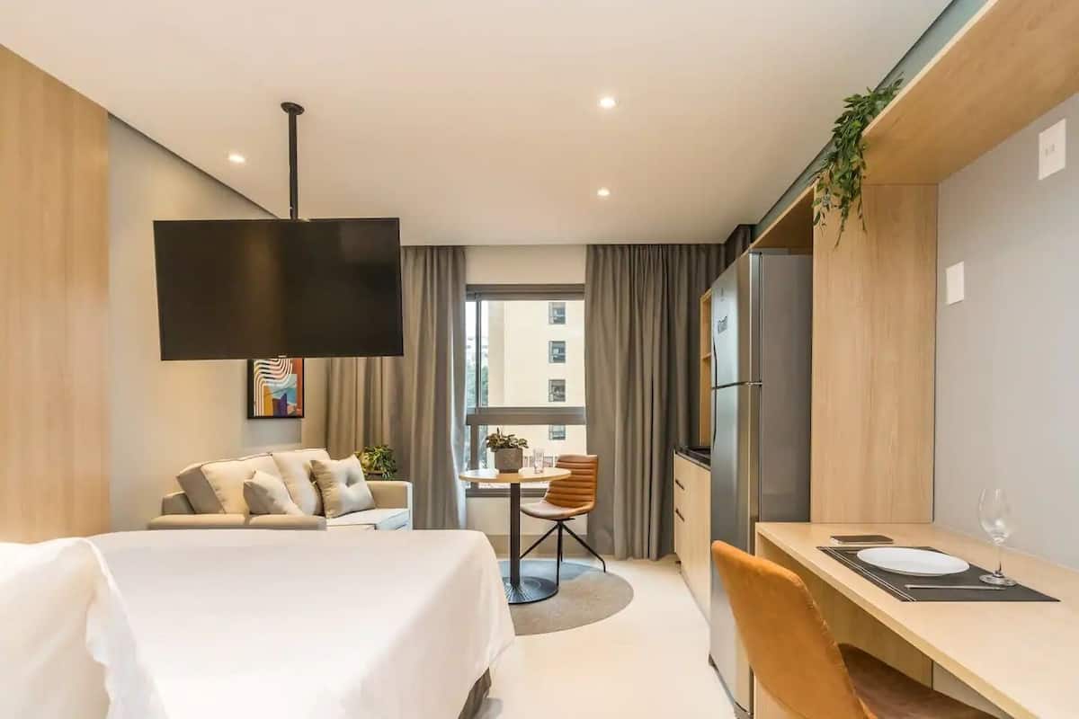 Une chambre d’hôtel moderne équipée d’un lit, d’un bureau, d’une chaise, d’une télévision et d’une fenêtre avec des rideaux.