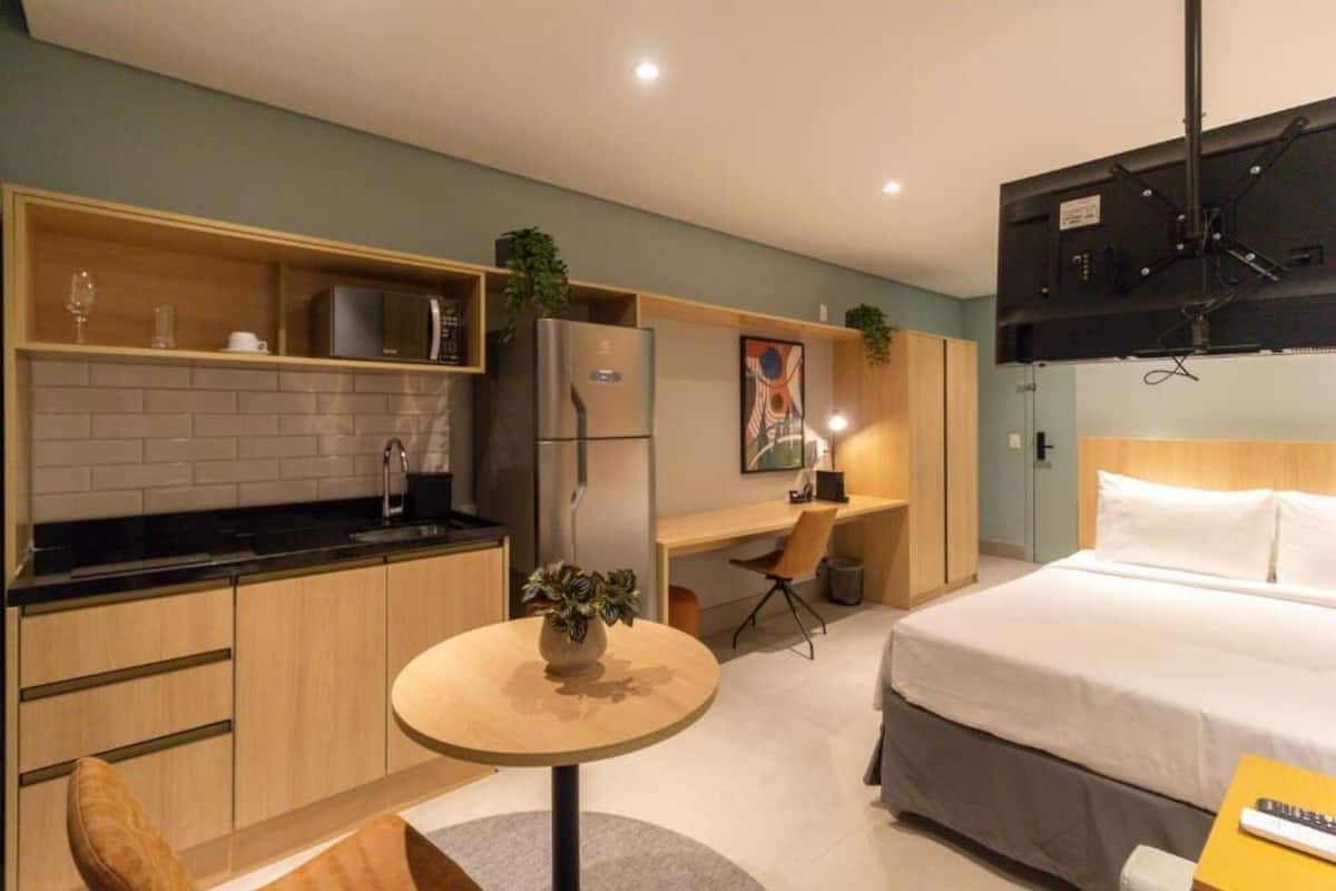 Une chambre d’hôtel de taille réduite, équipée d’une kitchenette, d’un lit, d’un bureau et d’une télévision.