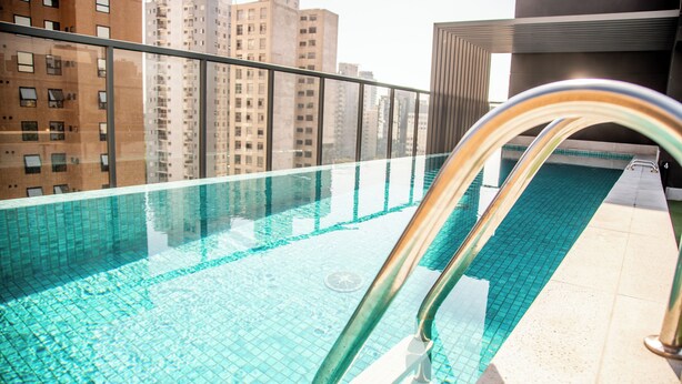 A rooftop pool with clear blue water, metal railings, and a cityscape view in the background. - Cozzy Suites Paraiso Hotel (São Paulo)