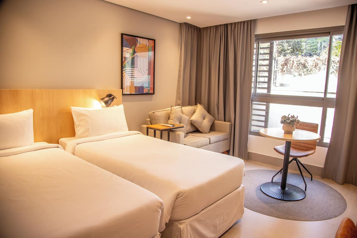 Une chambre d’hôtel avec deux lits, un canapé, une petite table et une fenêtre avec des rideaux.