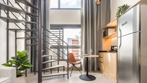 A modern kitchen with a stainless steel refrigerator, a dining table with a chair, and a staircase with metal railings. - Cozzy Suites Paraiso Hotel (São Paulo)