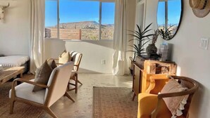 A room with a bed, a desk, a chair, and a large window with a view of a desert landscape. - Casa Flamingo | Cozy Cabin with Views | 5 Acres (Yucca Valley)