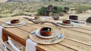A wooden table set outdoors with ceramic dishes and utensils, surrounded by desert vegetation and a clear sky. - Casa Flamingo | Cozy Cabin with Views | 5 Acres (Yucca Valley)