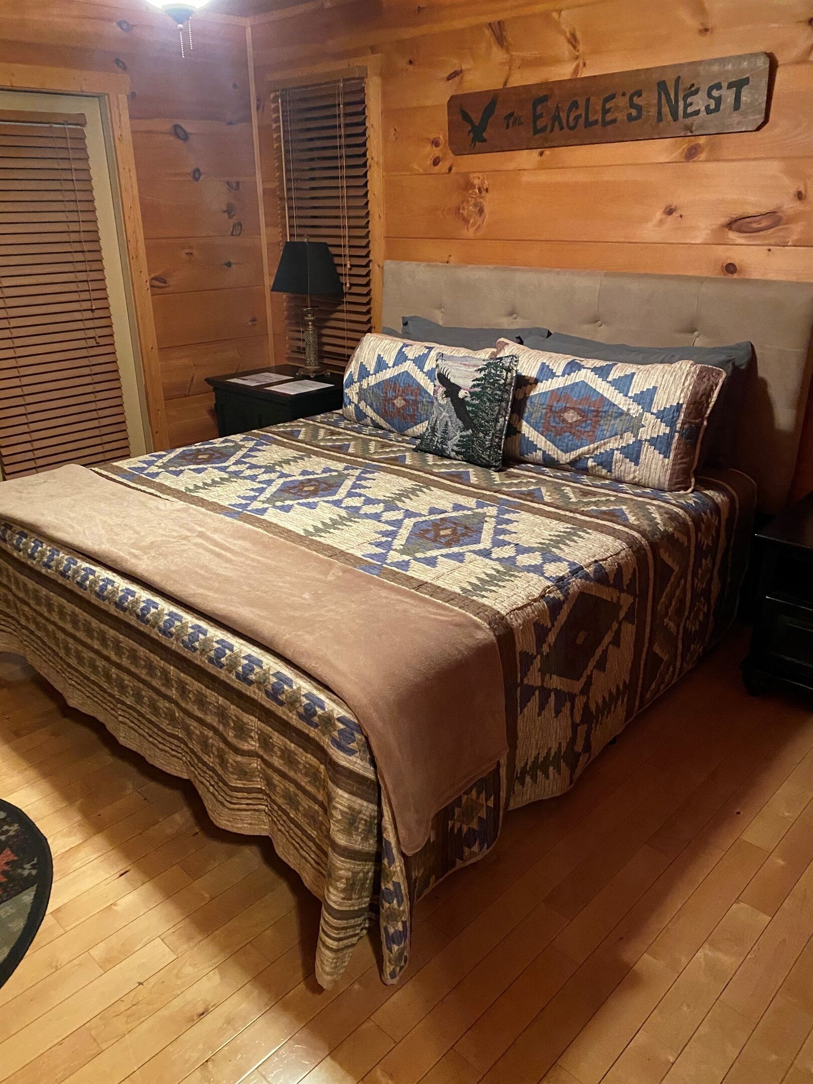 A wooden cabin interior with a bed, a nightstand, a lamp, and a sign reading "The Eagle's Nest".