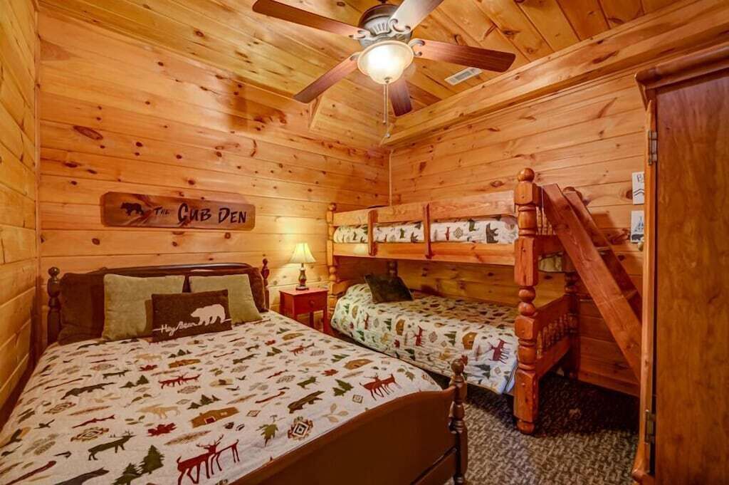 Et hytte-inspireret værelse med to køjesenge, en ventilator i træloft og et skilt med teksten "The Cub Den".