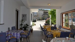 An outdoor dining area with tables and chairs, a view of the street, and a building in the background. - Room in Lopar with Terrace, Air condition, WIFI (3719-3) (Lopar)
