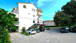 A multi-story building with a stone-paved entrance and several parked cars. - Room in Lopar with Terrace, Air condition, WIFI (3719-3) (Lopar)