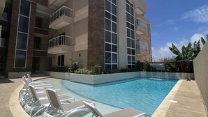 A modern building with a swimming pool, lounge chairs, and a clear blue sky. - Aracari Unit-4 Luxurious NEW Apartment (Noord)
