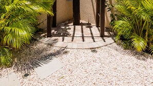 A covered entrance with a wooden pergola, surrounded by palm plants and a gravel pathway. - Aracari Unit-4 Luxurious NEW Apartment (Noord)