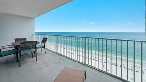Un balcón con mobiliario de mimbre, vista a una playa y cielo despejado.