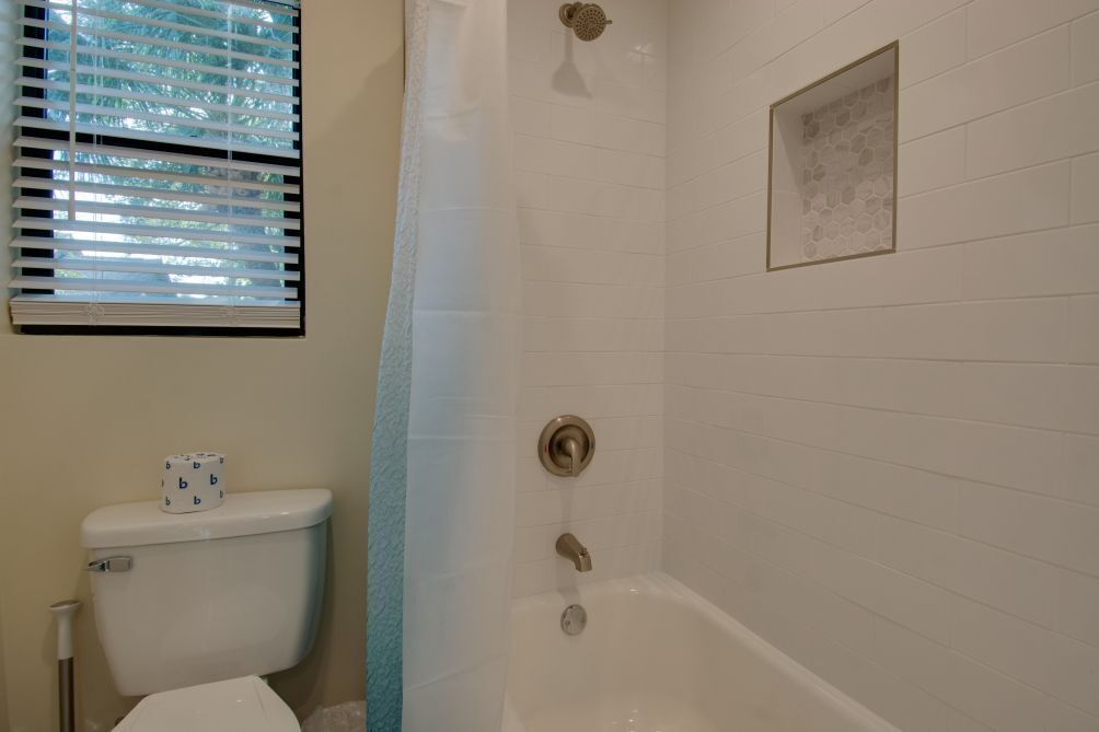 A bathroom with a toilet, shower, and a window with blinds.
