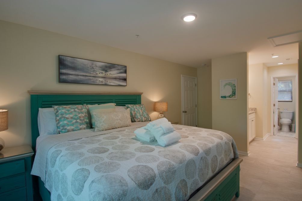 Un dormitorio con cama, mesita de noche, un cuadro en la pared y una puerta que da al baño.