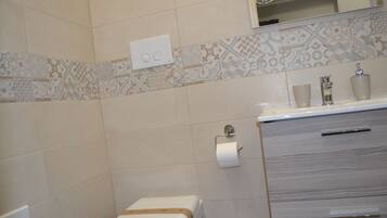 A bathroom with a toilet, a sink with a mirror above it, and patterned tiles on the wall.