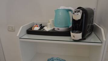 Una zona de cocina con cafetera, hervidor y microondas sobre una repisa de vidrio.