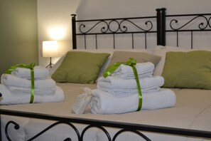 Una cama bien hecha con almohadillas verdes y toallas dobladas, una lámpara de noche y un cabecero de metal.