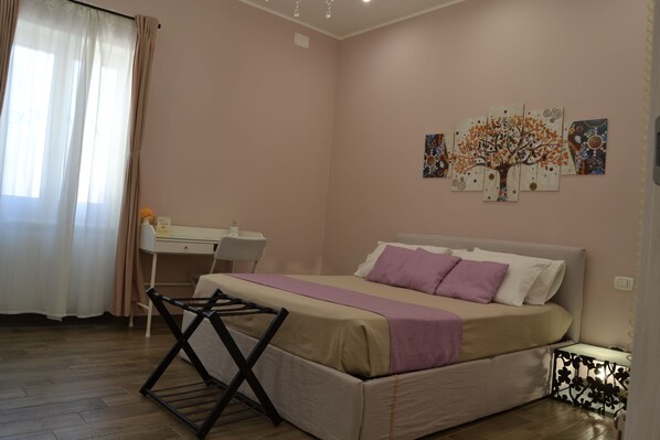 Un dormitorio con cama, escritorio y silla. Hay obras de arte en la pared sobre la cama.