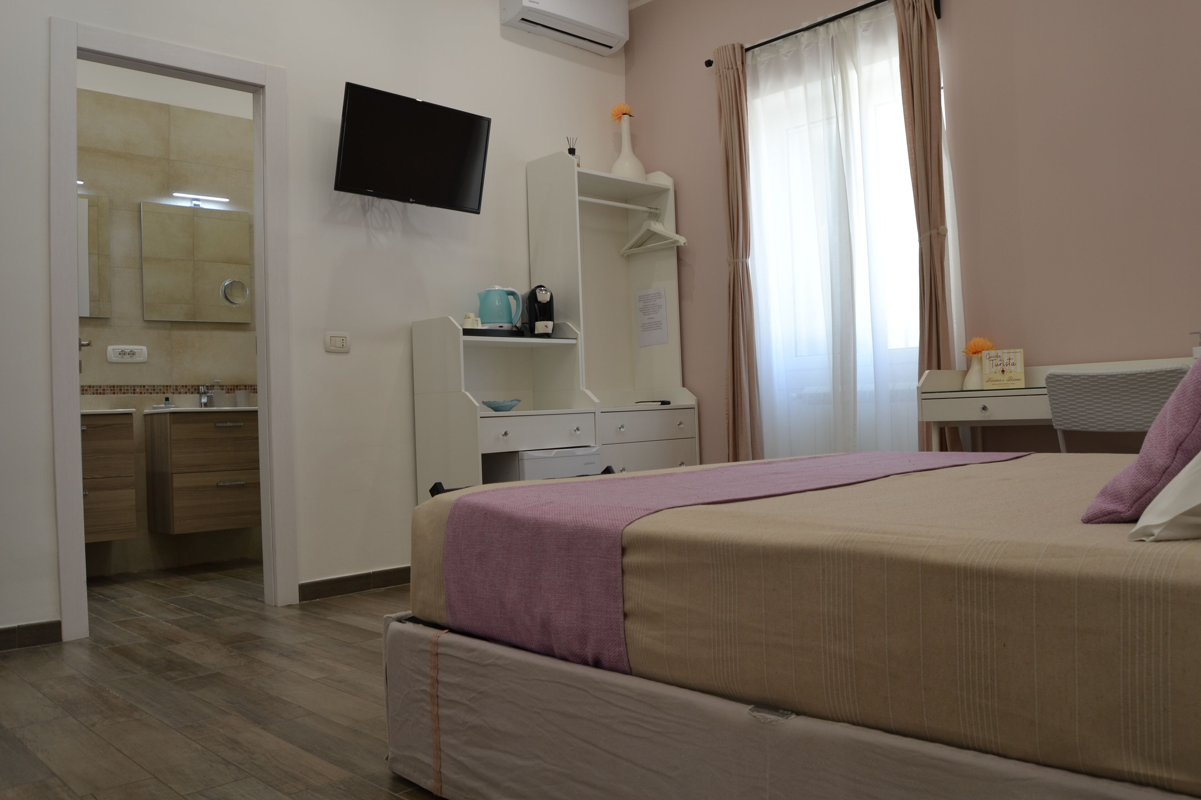 Ein Schlafzimmer mit einem Bett, einem an der Wand montierten Fernseher, einem Schreibtisch und einem durch eine offene Tür einsehbarer Badezimmer.