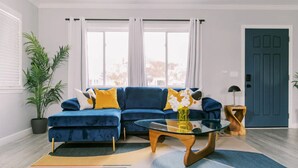 A modern living room with a blue sectional sofa, a glass coffee table, and a wooden side table. - Luxury Hangout | Private Spa + Game Room + Arcade (Long Beach)