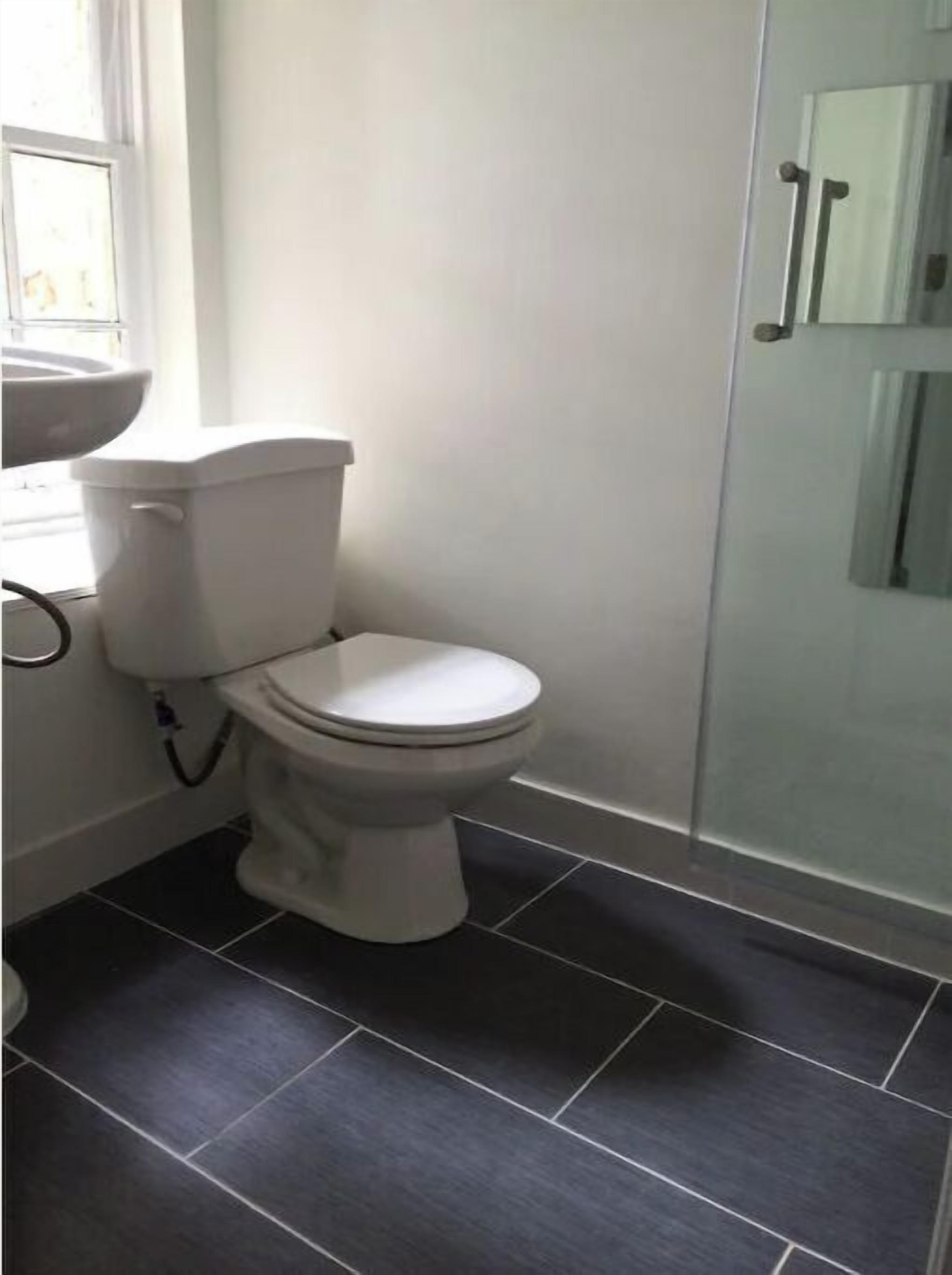 Une salle de bain avec des toilettes blanches, un carrelage foncé et une douche à parois de verre.