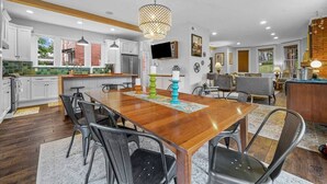 Une cuisine moderne avec des meubles blancs, une table à manger en bois et un luminaire suspendu.