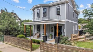 Une maison à deux étages avec un porche couvert, une pelouse devant et une clôture en bois.