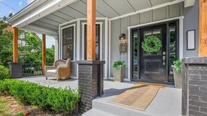 Un porche abrité avec une chaise, une porte décorée d’une guirlande et un jardinière.
