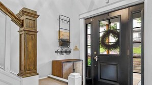 Une porte noire ornée d’une guirlande, un banc en bois et un porte-clés en métal.