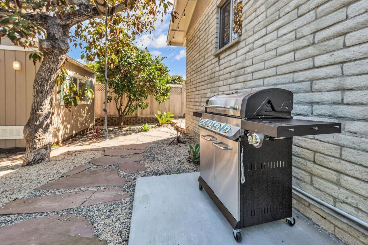 A backyard with a barbecue grill, a tree, and a house with a brick wall.
