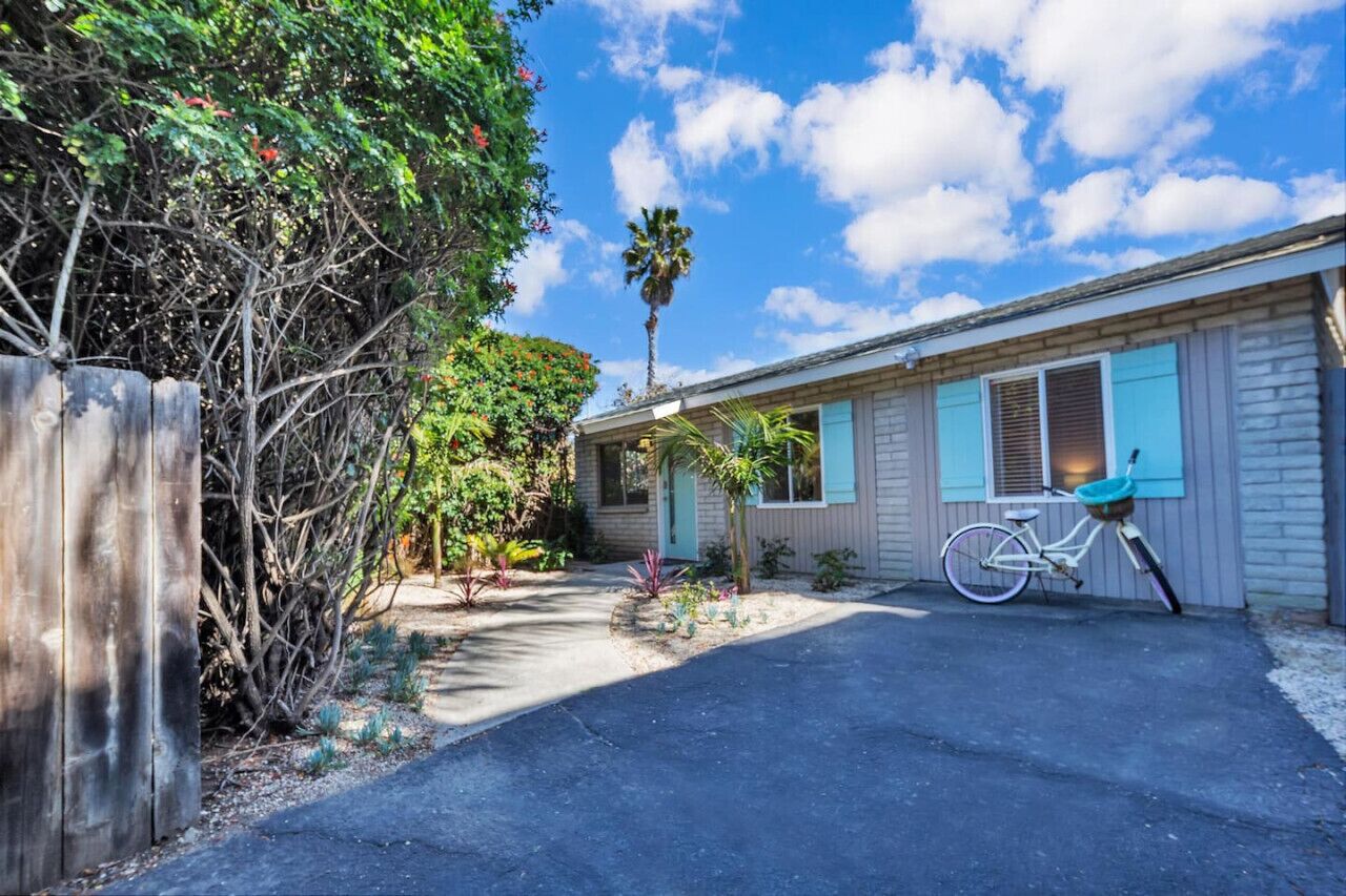 A residential house with a paved driveway, a bicycle, and a variety of plants and trees.