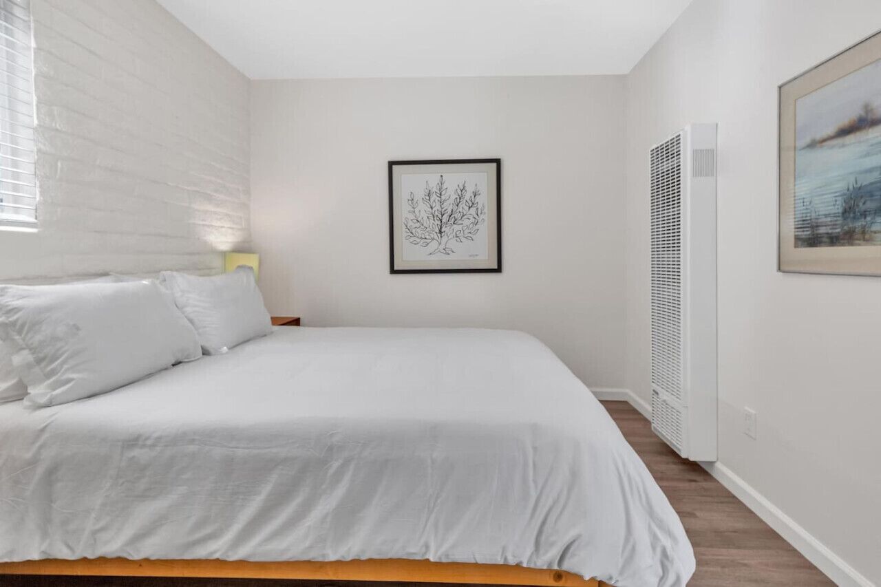 A bedroom with a bed, a framed artwork on the wall, and a window with blinds.