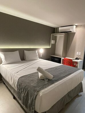 A hotel room with a large bed, a desk with a chair, a mirror, and an air conditioning unit. - Saint Patrick Grand Hotel (Maceió)